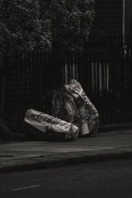 A pile of irregularly shaped waste materials consisting of white and grey plasterboard scraps, wood offcuts, and plastic packaging resting on a concrete driveway area. The trash is stacked in a disorg