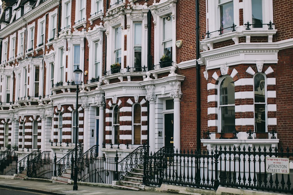 The image depicts the front entrance of a traditional brick terraced house with a small, enclosed front yard. There are two front doors, one painted in a muted blue-gray tone with a vertical glass pan