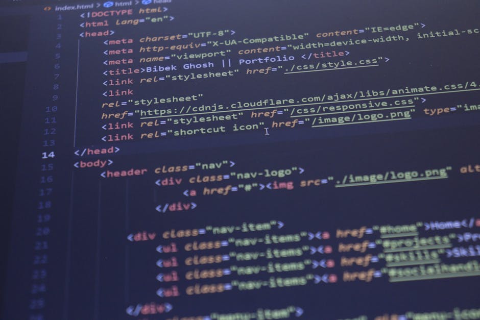 A person wearing a light blue shirt is seated at a desk, working on a laptop with a black screen displaying colorful lines of code in various programming languages. The individual's left hand is holdi